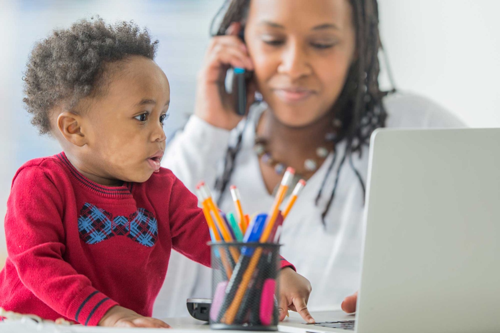 Woman on phone while young boy presses on computer keyboard
